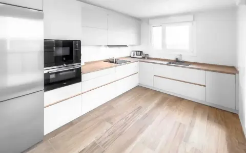 Cocina moderna con armarios blancos y encimeras de madera. El suelo de madera clara complementa perfectamente los suelos para cocinas blancas, creando un ambiente luminoso y acogedor.
