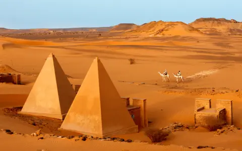 Pustynny krajobraz Sudanu z piramidami i dwoma podróżnikami na wielbłądach.