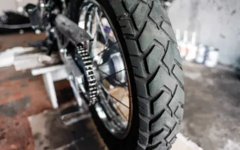 Zbliżenie na bieżnik motocyklowej opony, gotowej do wymiany. W tle widać fragment motocykla i narzędzia.