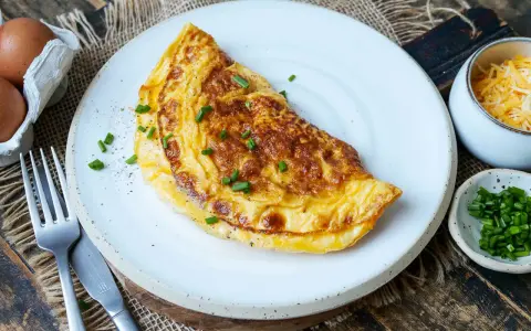 Goldbraunes Omelett mit Käse und Schnittlauch, perfekt für ein schnelles Omelette Rezept. Daneben Eier, Käse und Schnittlauch.