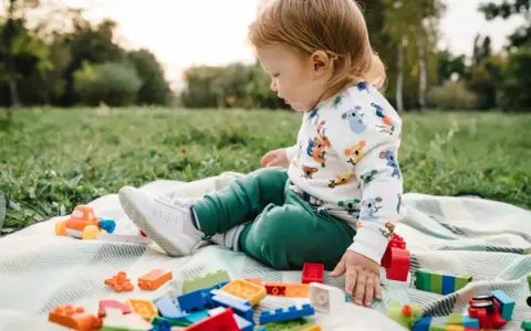 Un niño pequeño juega con bloques de construcción y un coche de juguete en el césped, disfrutando de actividades para niños de 2 a 3 años.