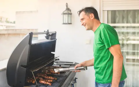 Glad man grillar korv på balkong.