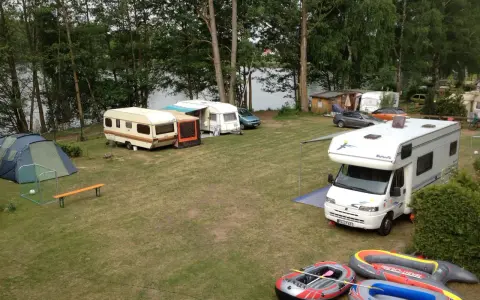 Campingplatz am sonnensee flachslanden mit Wohnmobilen, Wohnwagen, Zelt und Schlauchbooten am Ufer.