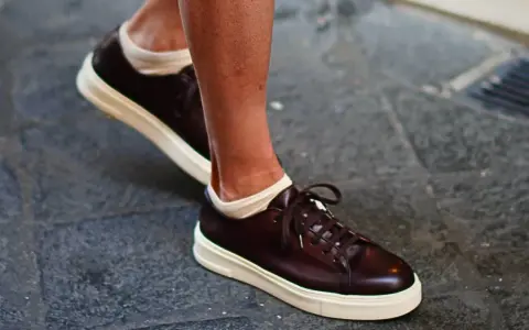 Un uomo indossa sneakers marroni con calze bianche a vista. Un look casual ma curato, perfetto per chi cerca quali calze con sneakers uomo.