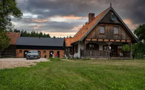 Szelągówka camping: drewniane domki i budynki gospodarcze, samochód na żwirowym podjeździe, zachmurzone niebo.