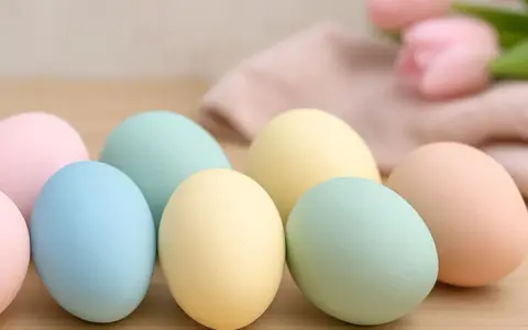 Huevos de pascua para pintar en tonos pastel, listos para decorar. Flores y tela suave al fondo.