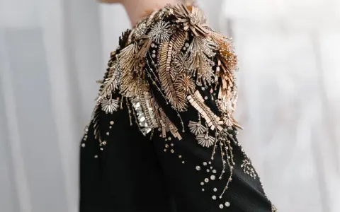 A black garment with an elaborate shoulder embellishment of gold and silver beads, sequins, and crystals, showcasing the definition of embellished fashion.