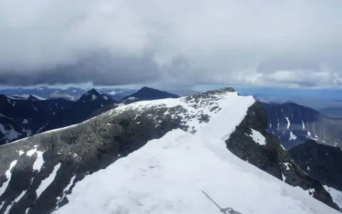 Snöklädda bergstoppar och molniga himlar. En repstump syns i förgrunden, redo för äventyret på Kebnekaise leder.