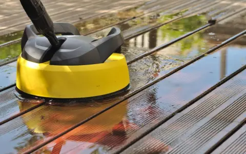 Nettoyer une terrasse en composite avec un nettoyeur haute pression. L'eau éclabousse sur les lattes de bois.