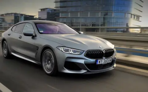 Srebrne BMW M850i sunie po moście, odbijając światła miasta w swoich szybach.