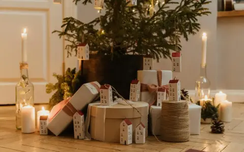 Julkalender tips: En julgran med små hus som dekorationer, presenter och ljus skapar en mysig julstämning.
