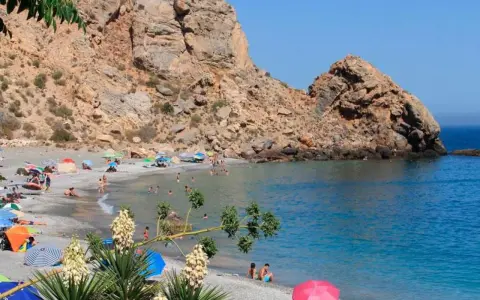 Playa de arena gris con gente disfrutando del sol y el mar, rodeada de acantilados. Un paraíso entre los pueblos de Granada con playa.