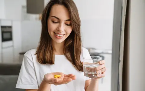Uśmiechnięta kobieta trzyma w dłoni tabletki preductal mr 35 mg i szklankę wody.