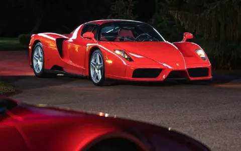 Czerwone Ferrari Enzo zaparkowane nocą na drodze, z innym czerwonym samochodem w tle.