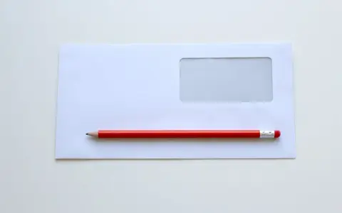 Biała koperta z okienkiem i czerwony ołówek. Proste narzędzia, by dowiedzieć się, jak wypełnić kopertę do wysłania.