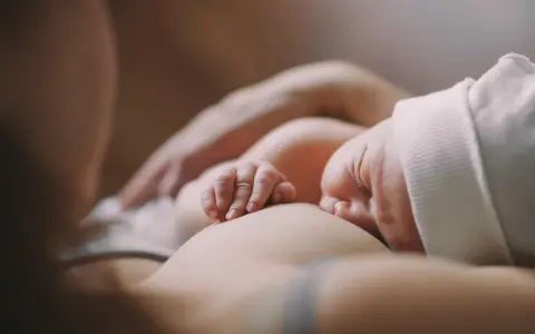 Ein Baby stillt, die kleinen Finger greifen sanft zu. Ein Moment der Ruhe und Verbundenheit.