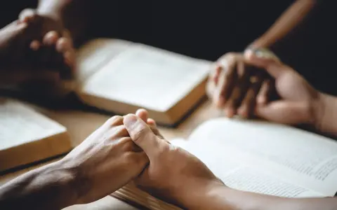 Hände halten sich über aufgeschlagenen Bibeln, ein Zeichen dafür, wie beten Christen: in Gemeinschaft, mit Glauben und Hoffnung.