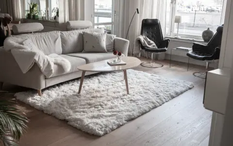 En fluffig, vit matta ligger framför en ljusgrå soffa och skapar en mysig känsla i vardagsrummet.