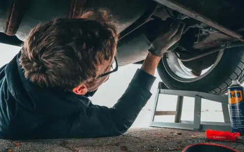Un giovane impara come si diventa meccanico, lavorando sotto un'auto con attrezzi e spray.