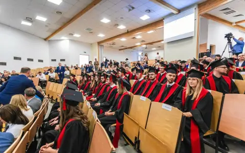 Absolwenci w togach siedzą na uroczystości w sali wykładowej. To ważny dzień dla studentów z Radomia.