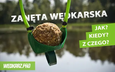 Kula zanęty wędkarskiej 5 kg w zielonej łopatce, gotowa do zarzucenia. W tle woda i drzewa.
