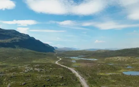 Väg slingrar sig genom ett vidsträckt landskap med berg och sjöar. Perfekt för camping i Norrbotten.