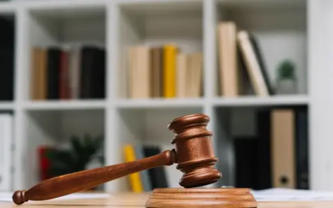 Młotek sędziowski na biurku, symbol prawa. W tle regał z książkami. Jak wyegzekwować alimenty od niepracującego ojca? Prawo jest po Twojej stronie.