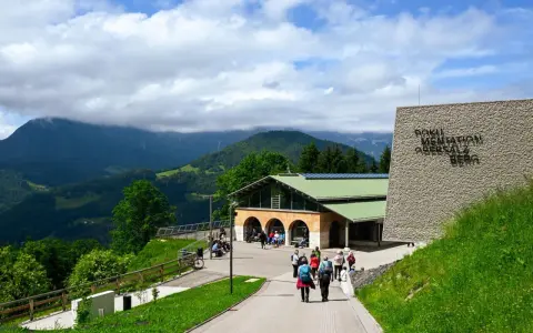 Besucher erkunden das Dokumentationszentrum Obersalzberg, umgeben von grünen Hügeln und Bergen.