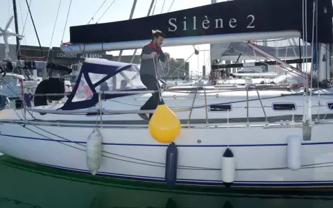 Un homme ajuste un pare-battage jaune sur un voilier. Ces bouées protègent la coque des chocs.
