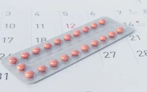 Różne rodzaje tabletek antykoncepcyjnych w blistrze na tle kalendarza.