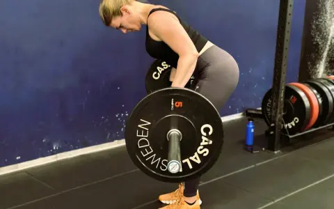 Kvinna utför en t bar row med en skivstång i ett gym.