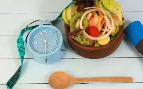 Réveil bleu, ruban à mesurer, salade fraîche et haltère bleu. L'heure est à la forme, jeune 16/8.