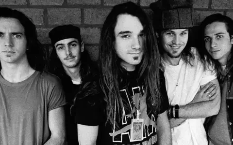 Cinq membres du groupe Pearl Jam posent devant un mur de briques. L'un d'eux porte un t-shirt avec le logo du groupe.