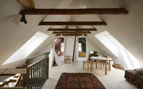 Idee per ristrutturare casa antica: mansarda luminosa con travi a vista, tappeto persiano, teepee e tavolino per bambini.