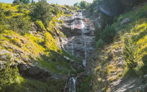Cascada cayendo por una ladera rocosa, rodeada de vegetación verde y amarilla. Un hermoso paisaje que invita a recorrer la ruta de las tres cascadas.