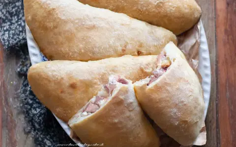 Calzoni al forno dorati e fragranti, ripieni di prosciutto e formaggio filante, pronti per essere gustati.