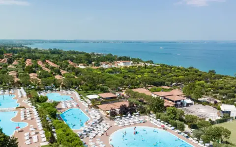 Widok z lotu ptaka na camping Piani di Clodia z basenami, domkami i jeziorem w tle.