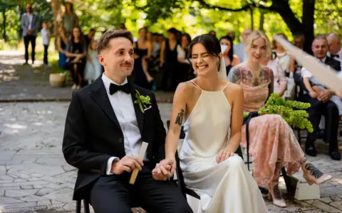 Szczęśliwa para podczas ślubu cywilnego w plenerze. Panna młoda śmieje się, pan młody trzyma wachlarz.