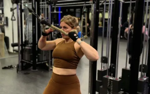 Kvinna utför stående rodd med kabelmaskin. Hon fokuserar på träningen i gymmet.