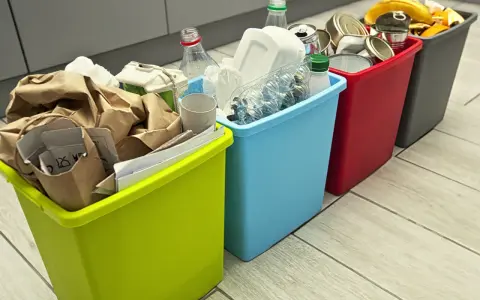 Cztery kolorowe kosze na śmieci z posegregowanymi odpadami: papier, plastik, metal i bio.