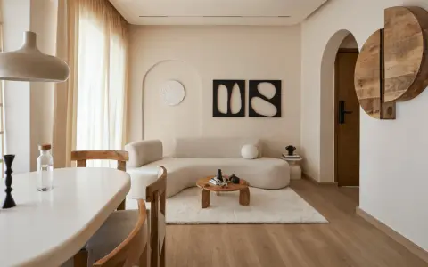 Un soggiorno in stile wabi sabi arredamento, con divano curvo, tavolino in legno grezzo, tappeto soffice e decorazioni organiche.