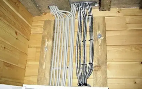 Instalacja elektryczna w domu drewnianym schemat: wiązki kabli w peszlach wychodzące z sufitu, przymocowane do drewnianych belek.
