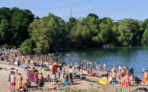 Ein sonniger Tag am **Badesee Bonn**. Viele Menschen genießen das Wasser und den Strand, umgeben von grünen Bäumen.