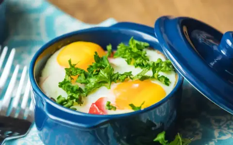 Un délicieux oeuf cocotte, parsemé de persil frais, prêt à être dégusté avec une fourchette.