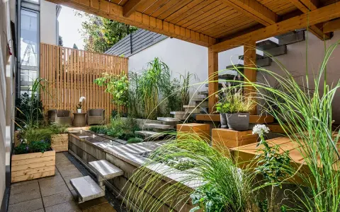Giardini fioriti idee: un angolo zen con vasca d'acqua, gradini in pietra, sedute in legno e piante rigogliose sotto un pergolato.