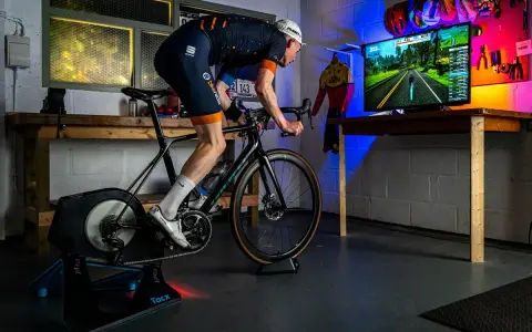 A cyclist trains indoors on a bike trainer, with a screen showing a virtual road. This setup demonstrates how to set up a bike trainer for immersive cycling.