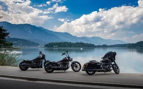 Tre moto parcheggiate sul lungolago, pronte per il faaker see motoraduno. Montagne sullo sfondo, cielo azzurro con nuvole bianche.
