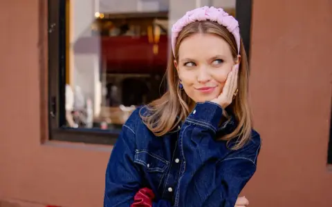Aesthetic girl w różowej opasce i dżinsowej kurtce, opierająca głowę na dłoni, zamyślona.