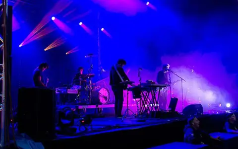 Un groupe allemand des années 2010 joue sur scène sous des lumières bleues et violettes.