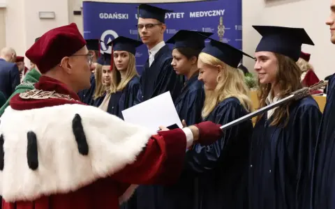 Uroczystość wręczenia dyplomów na studiach w Trójmieście. Absolwenci w togach odbierają gratulacje.